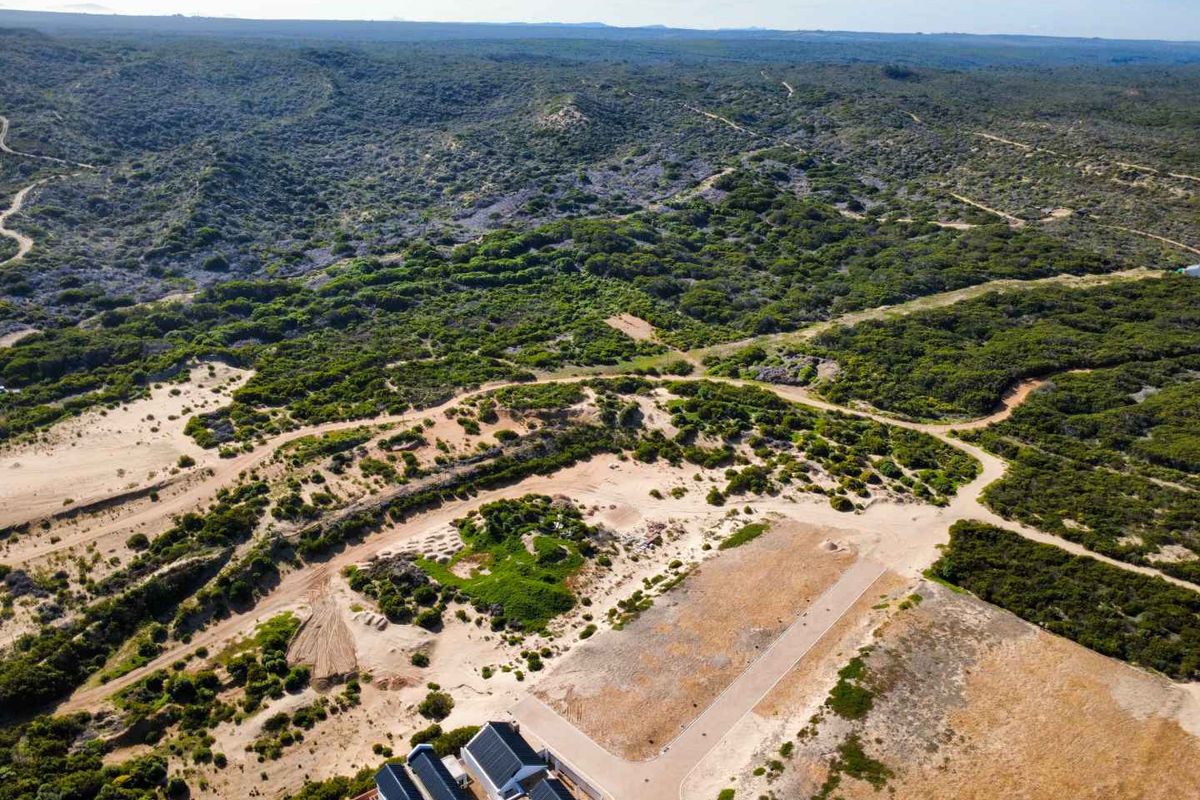 Aerial view of a residential land plot featuring natural coastal vegetation, sand dunes, and access to a paved road.