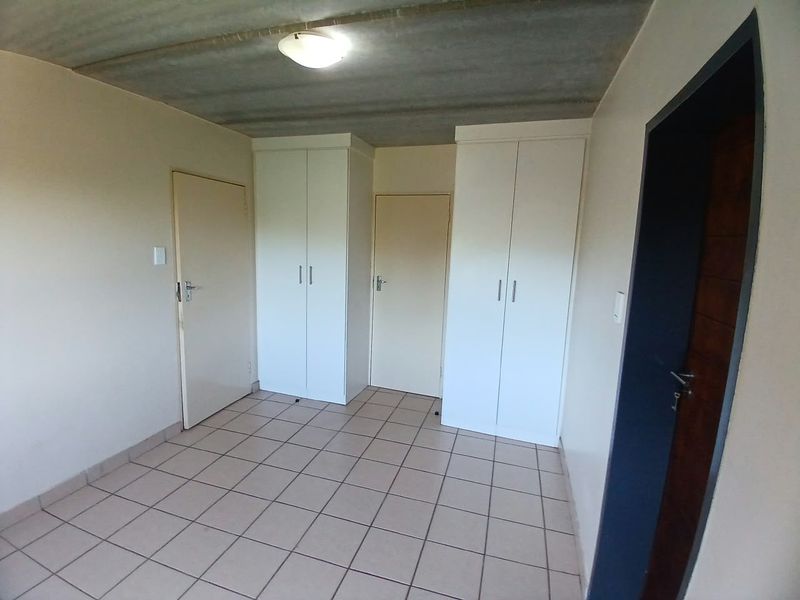 An empty bedroom featuring tiled flooring, built-in cupboards, and an exposed concrete ceiling.