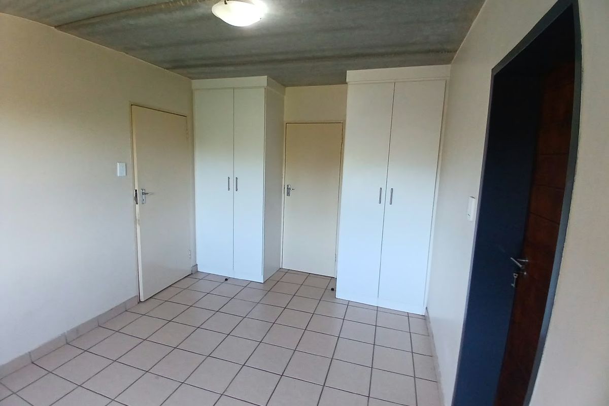 An empty bedroom featuring tiled flooring, built-in cupboards, and an exposed concrete ceiling.