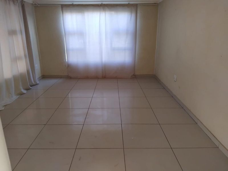 An empty living room featuring neutral ceramic floor tiles and plain walls, providing a blank canvas for interior design and personalization.