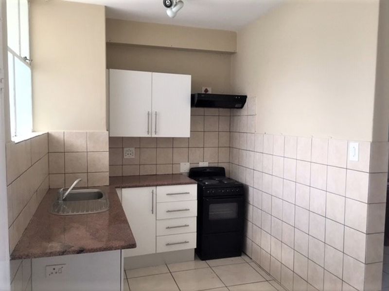 A compact kitchen featuring granite countertops, white cabinetry, a tiled splashback, and a freestanding stove, offering a functional space ready for updates.