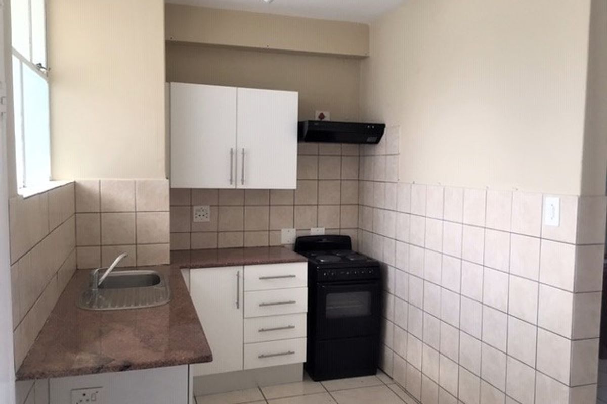 A compact kitchen featuring granite countertops, white cabinetry, a tiled splashback, and a freestanding stove, offering a functional space ready for updates.