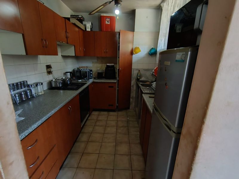 A functional kitchen featuring wood-tone cabinetry, laminate countertops, tiled backsplash, and ceramic flooring, offering a practical layout with built-in cooking appliances.