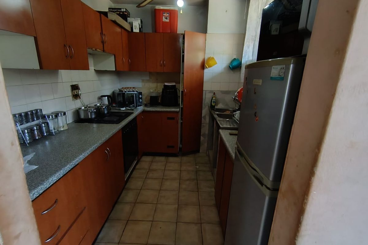 A functional kitchen featuring wood-tone cabinetry, laminate countertops, tiled backsplash, and ceramic flooring, offering a practical layout with built-in cooking appliances.