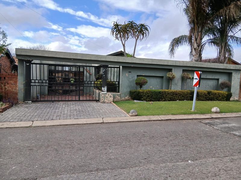 Front view of the property featuring a perimeter wall, metal security gate, and paved driveway area.