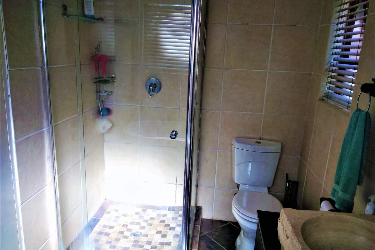 A functional bathroom featuring a glass-enclosed shower, a standard toilet, and a unique stone basin with tiled walls and flooring.