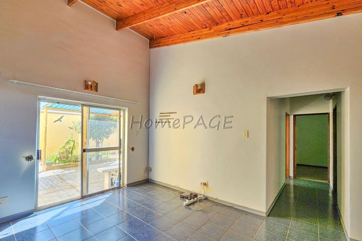 An open-plan living area featuring tiled flooring, a high timber-clad ceiling, and sliding glass doors providing direct access to the rear patio.