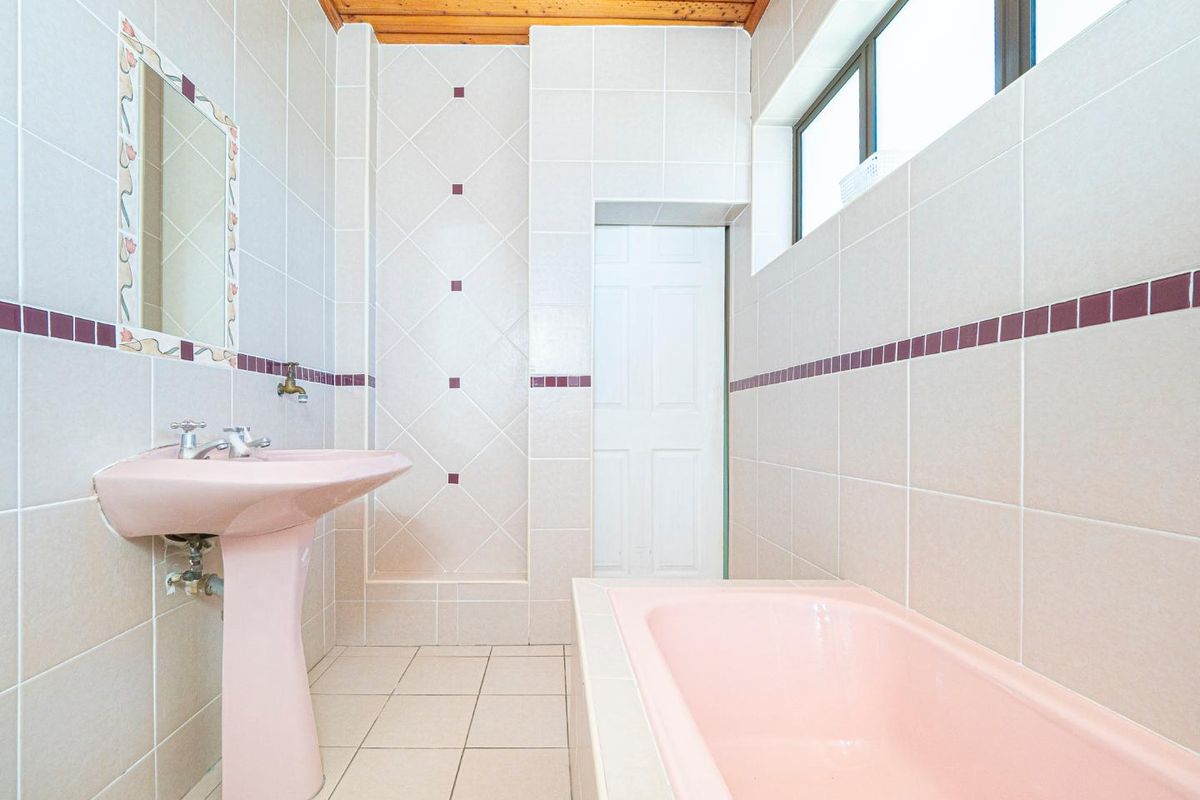 A dated bathroom featuring pink pedestal basin and built-in bathtub, tiled walls and flooring, and a timber-paneled ceiling.