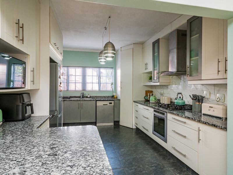 A well-appointed kitchen featuring granite countertops, built-in oven, gas hob, stainless steel extractor fan, and ample cabinetry with a functional layout.