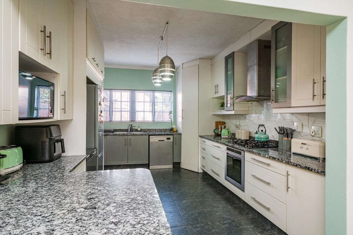 A well-appointed kitchen featuring granite countertops, built-in oven, gas hob, stainless steel extractor fan, and ample cabinetry with a functional layout.