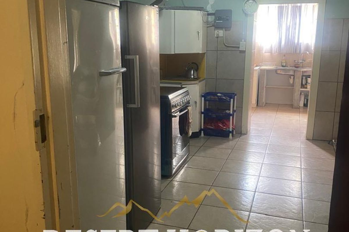 A functional kitchen area featuring tiled flooring and a connected scullery, requiring cosmetic updates and wall repairs.