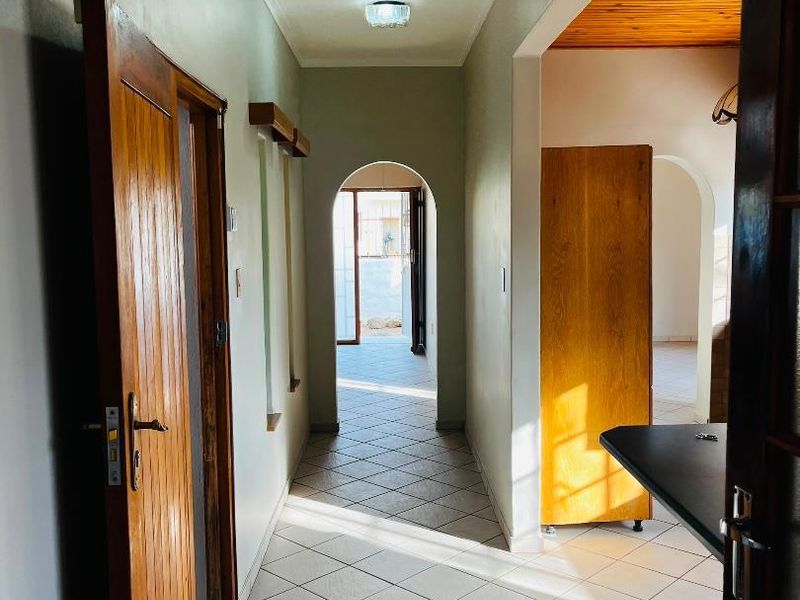 A bright, tiled hallway featuring classic archways and wooden door frames, providing a clear transition between living spaces.