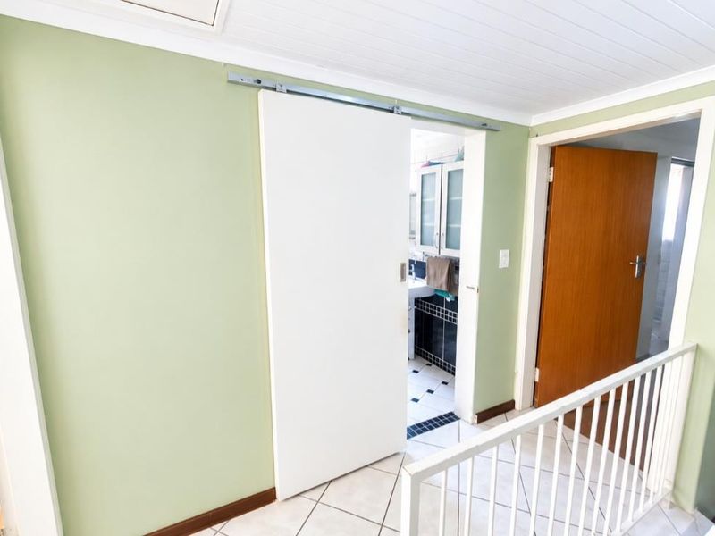A bright hallway featuring tiled flooring, a white sliding door, and a metal balustrade overlooking the lower level.