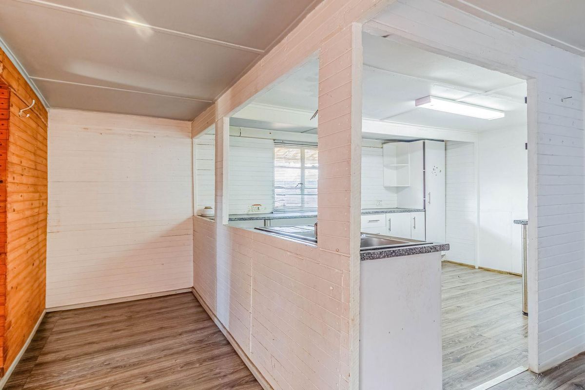 A functional kitchen area featuring timber wall paneling, laminate flooring, and a pass-through window connecting to the adjacent living space.