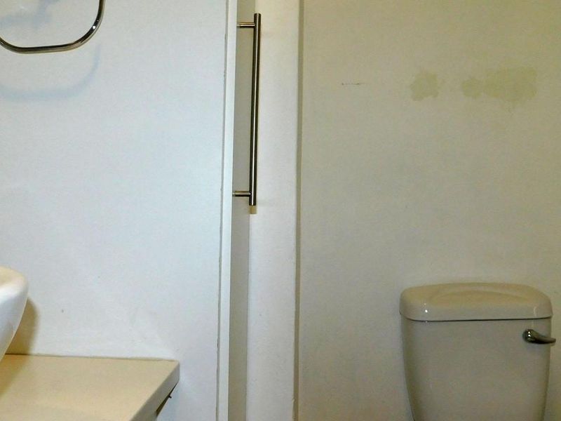 A compact bathroom featuring a vessel sink, toilet, and wall-mounted grab bar, showing signs of wear on the wall surfaces.