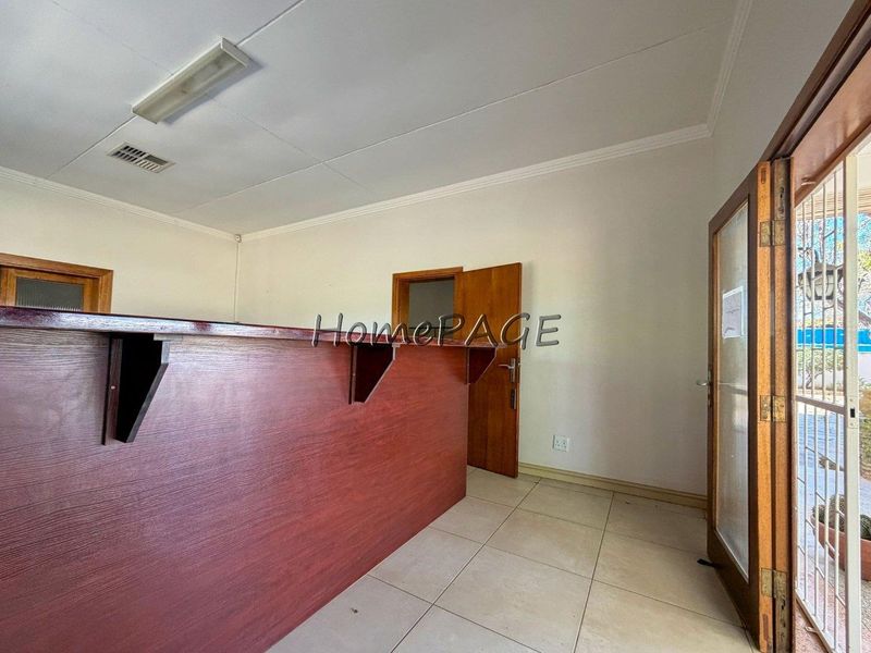 An empty room featuring a built-in wooden bar counter, tiled flooring, and direct access to an outdoor area through a glass-paneled wooden door.