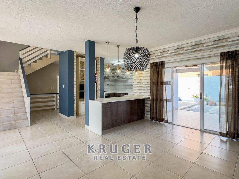 Spacious open-plan living area featuring a kitchen island, stone veneer accents, tiled flooring, and direct access to the patio through sliding glass doors.