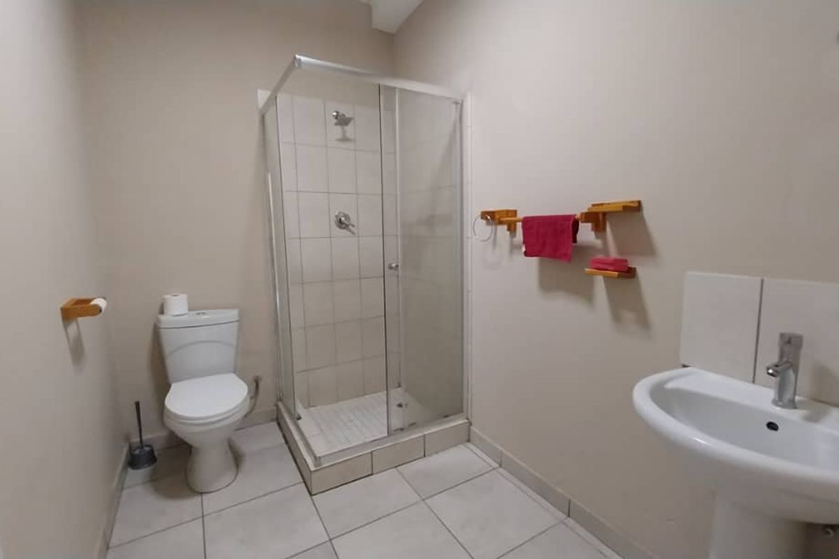 A functional bathroom featuring a glass-enclosed shower, pedestal basin, and toilet with neutral floor tiling.