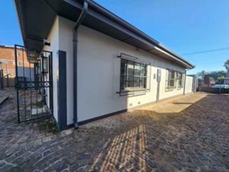 Exterior view of the property featuring paved ground, security bars on windows, and metal security gate access.