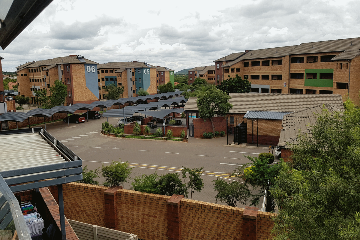 Elevated view of the apartment complex grounds, featuring paved parking areas with covered carports, brick boundary walls, and landscaped surroundings.