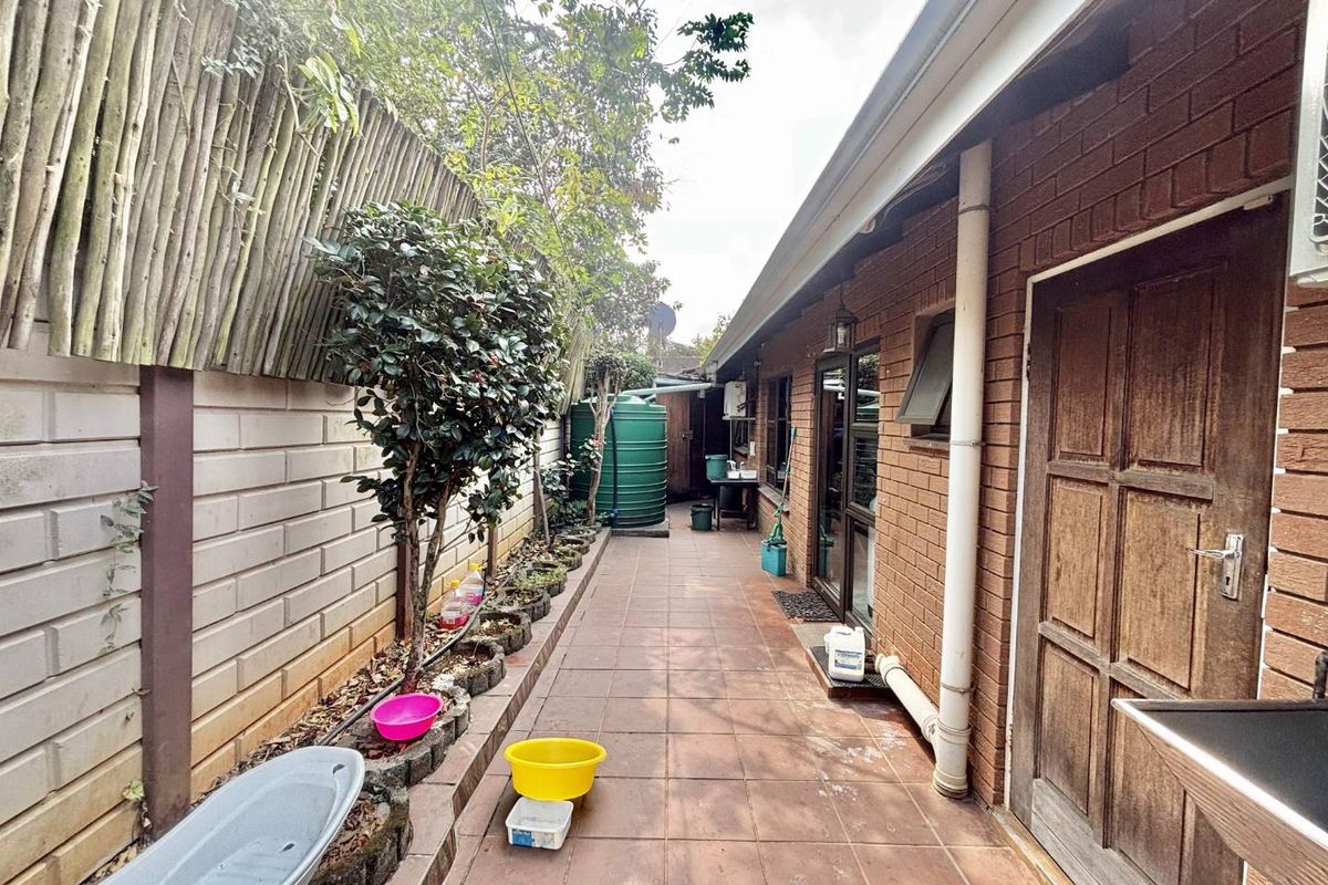 A narrow rear exterior walkway featuring tiled flooring, a brick facade, and a water tank, providing access along the side of the property.