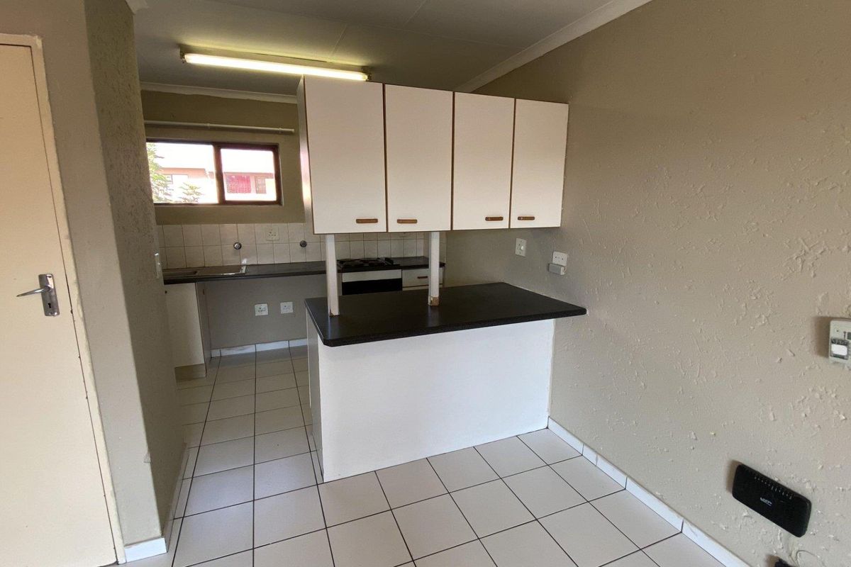 A functional, empty kitchen featuring tiled flooring, built-in cabinetry, a breakfast counter, and a built-in oven, offering a blank canvas for modern updates.