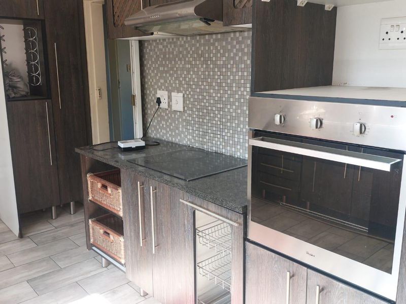 A functional kitchen featuring dark wood-look cabinetry, granite countertops, a mosaic tile backsplash, and integrated appliances including an oven and electric hob.