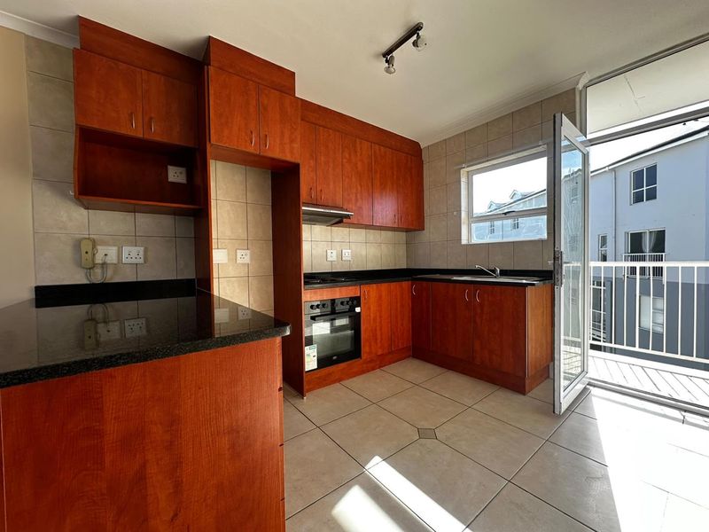 A functional kitchen featuring cherry-wood cabinetry, granite countertops, built-in oven and hob, and direct access to a private balcony.