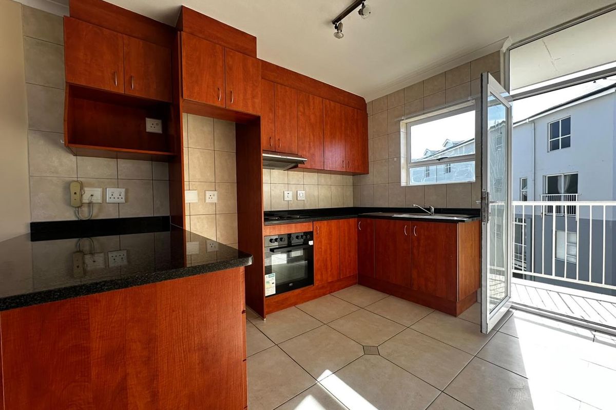 A functional kitchen featuring cherry-wood cabinetry, granite countertops, built-in oven and hob, and direct access to a private balcony.