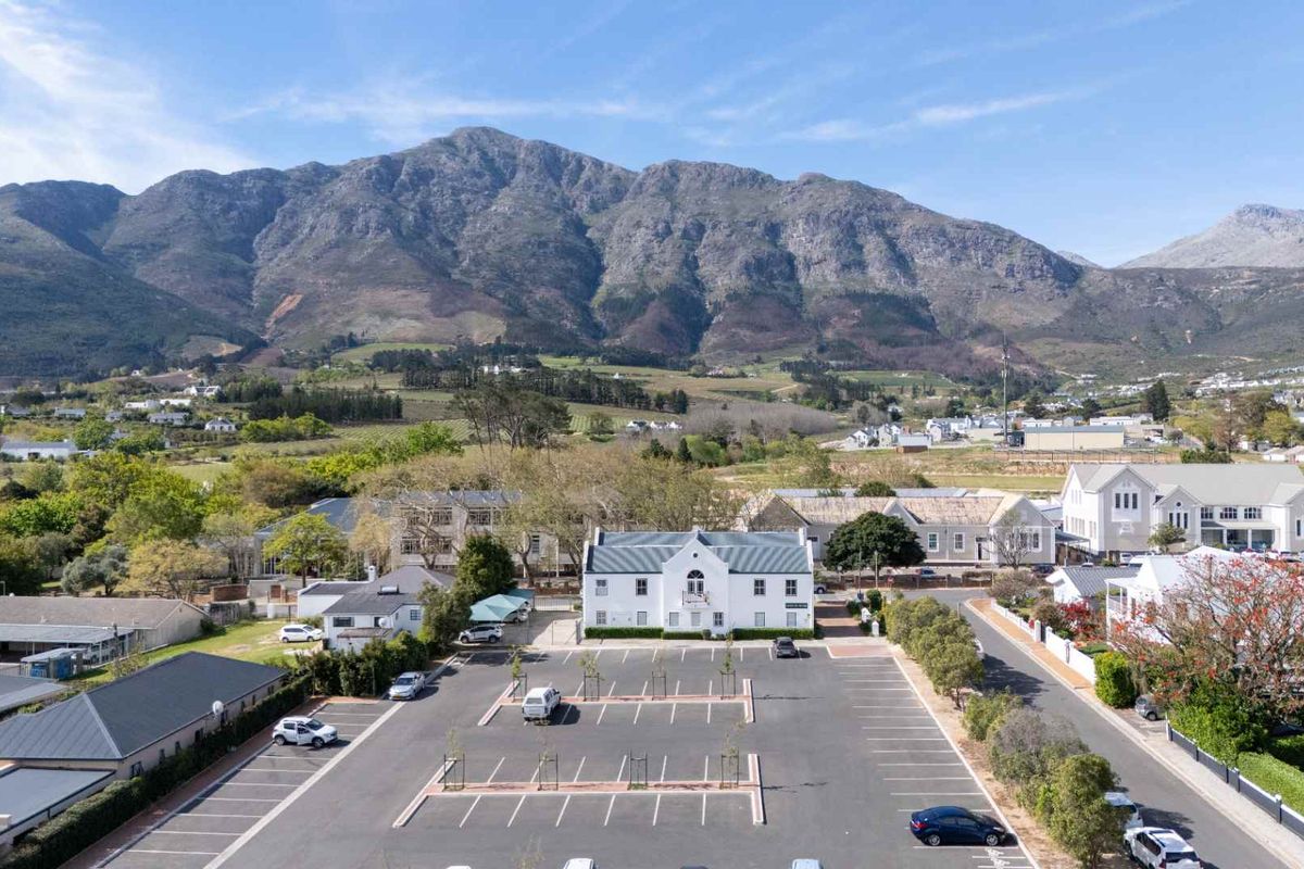 Aerial view of a commercial property featuring a large asphalt parking area, surrounding landscaped grounds, and a prominent building set against a mountain backdrop.