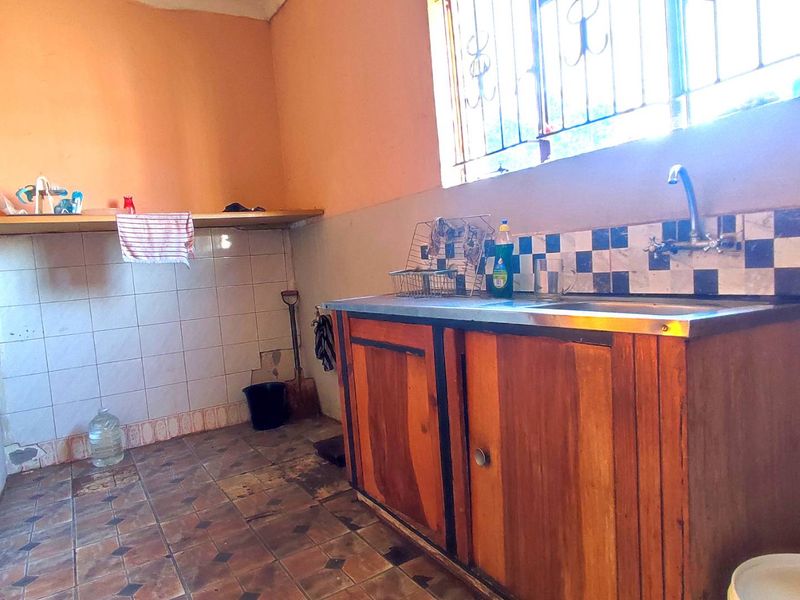A basic kitchen area featuring a stainless steel sink, wooden cabinetry, and tiled splashback, requiring significant renovation and cosmetic updates.