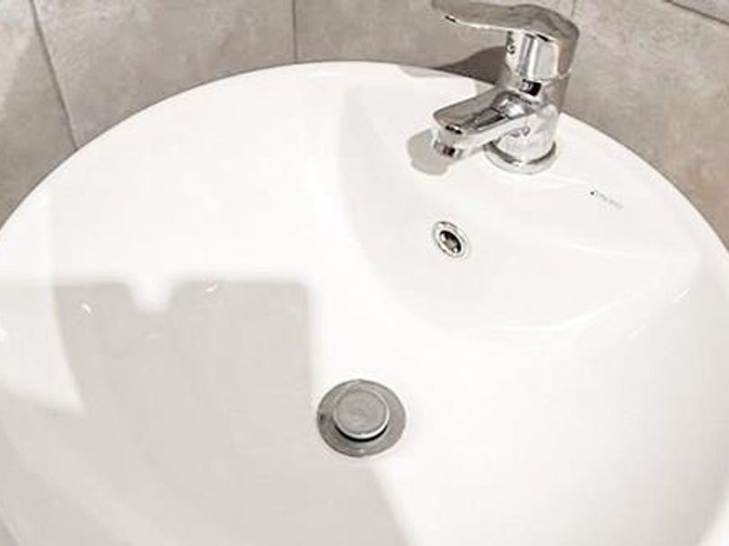 A close-up view of a modern white ceramic bathroom basin featuring a chrome mixer tap and neutral tiled splashback.