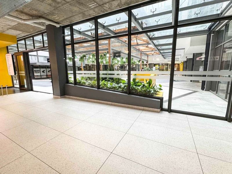 Modern retail space featuring large glass storefront windows, polished tile flooring, and an exposed concrete ceiling with views into a bright, skylit atrium.