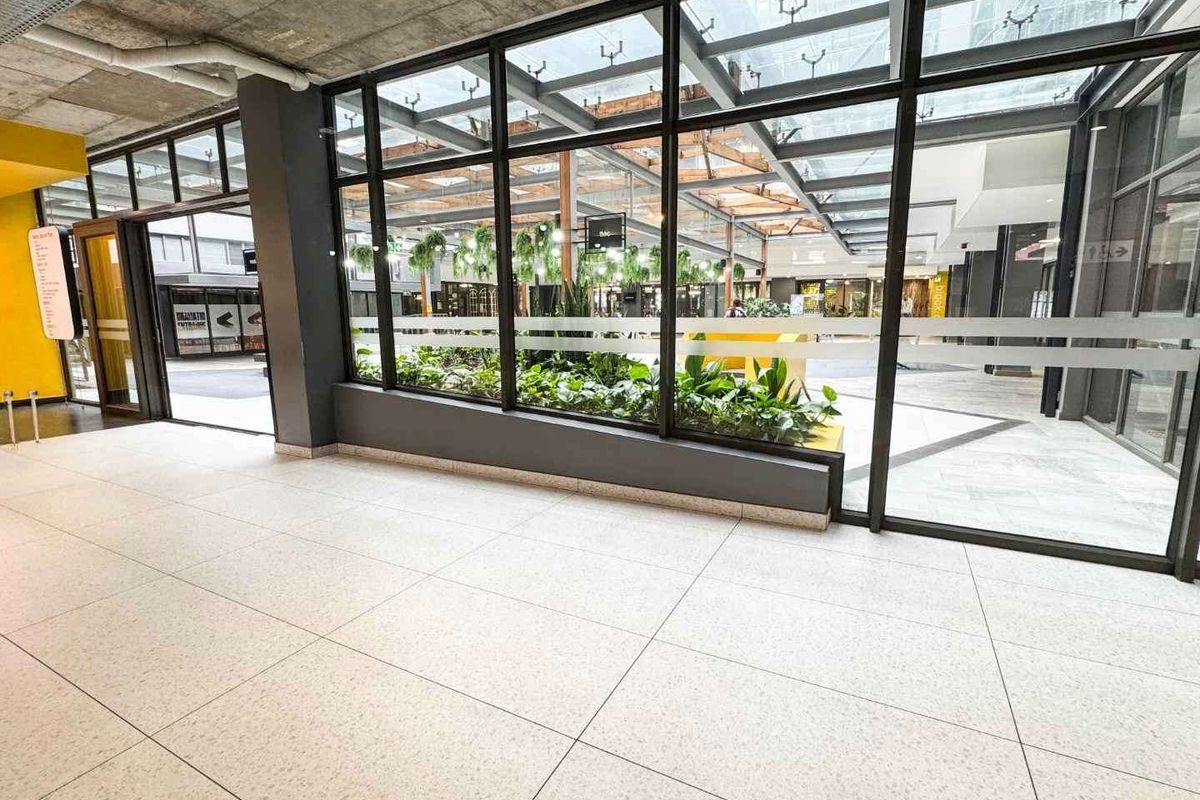 Modern retail space featuring large glass storefront windows, polished tile flooring, and an exposed concrete ceiling with views into a bright, skylit atrium.