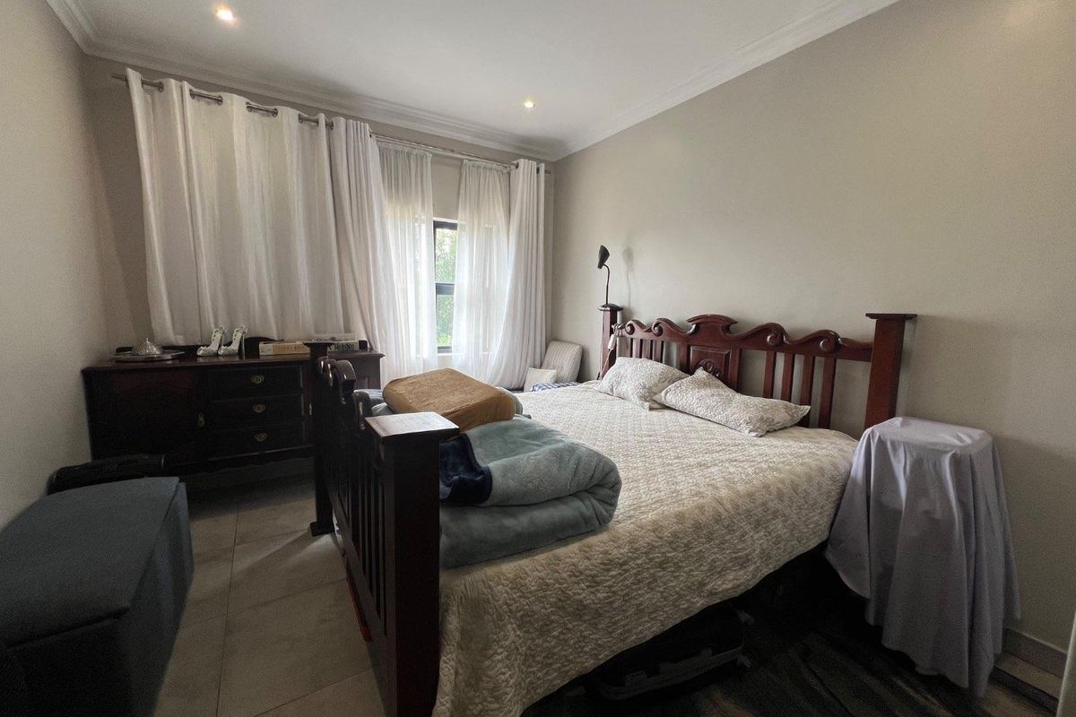 A spacious bedroom featuring neutral wall tones, tiled flooring, recessed ceiling lighting, and large windows dressed with floor-to-ceiling curtains.