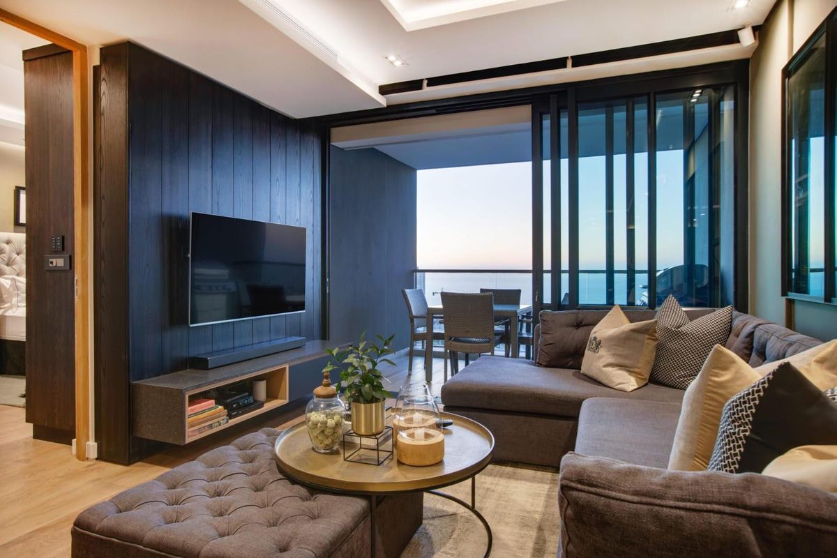 Modern living room featuring dark timber wall paneling, recessed ceiling lighting, and seamless access to an outdoor balcony with ocean views.