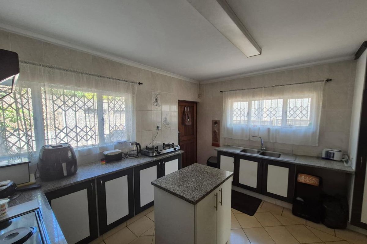 A functional kitchen featuring granite countertops, a central island, double basin sink, and ample built-in cabinetry with security bars on the windows.
