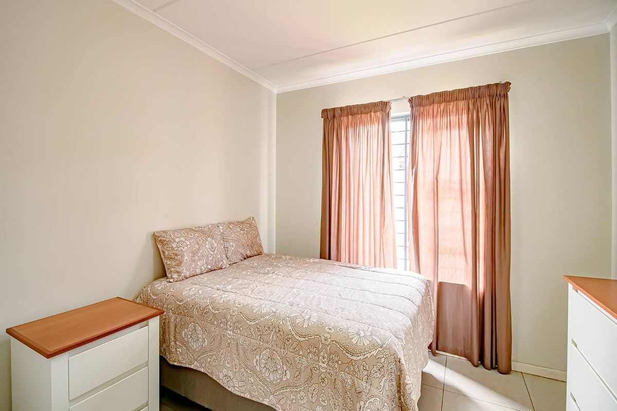 A functional bedroom featuring tiled flooring, neutral wall finishes, and a window with security bars and curtains.