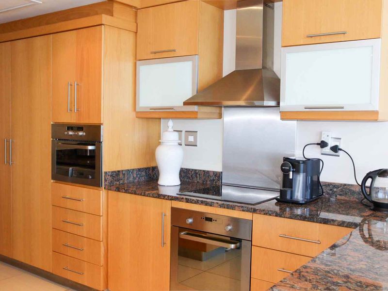A functional kitchen featuring light wood cabinetry, granite countertops, a built-in oven, electric hob, and stainless steel extractor fan.