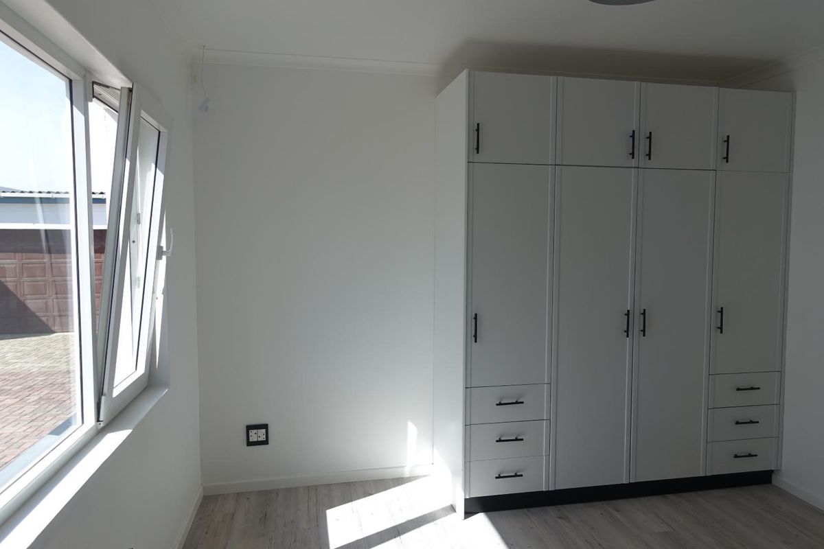 A bright bedroom featuring modern built-in white cabinetry with integrated drawers and a large window providing natural light.