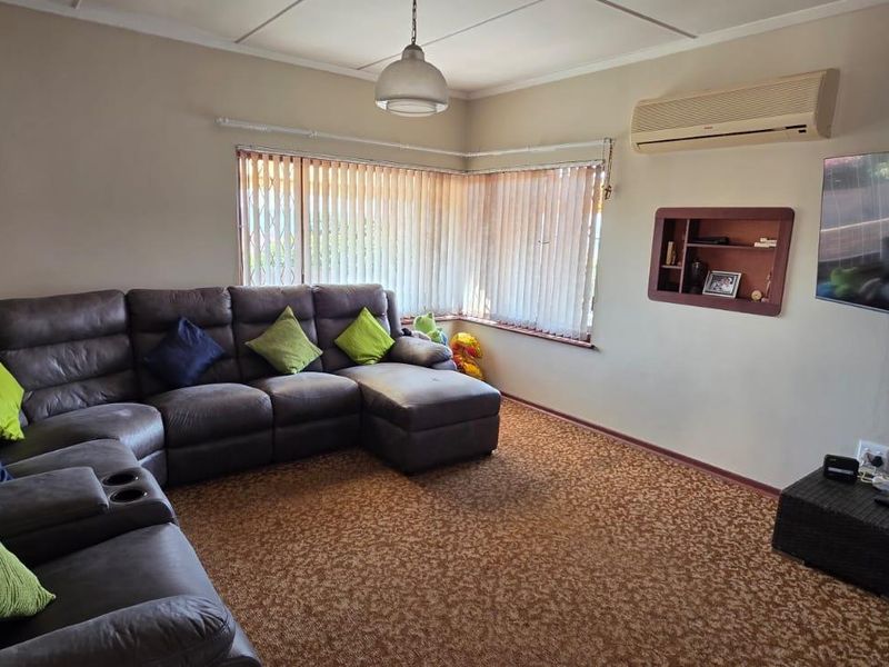 A comfortable living room featuring carpet flooring, a wall-mounted air conditioning unit, and a built-in wall niche for display.
