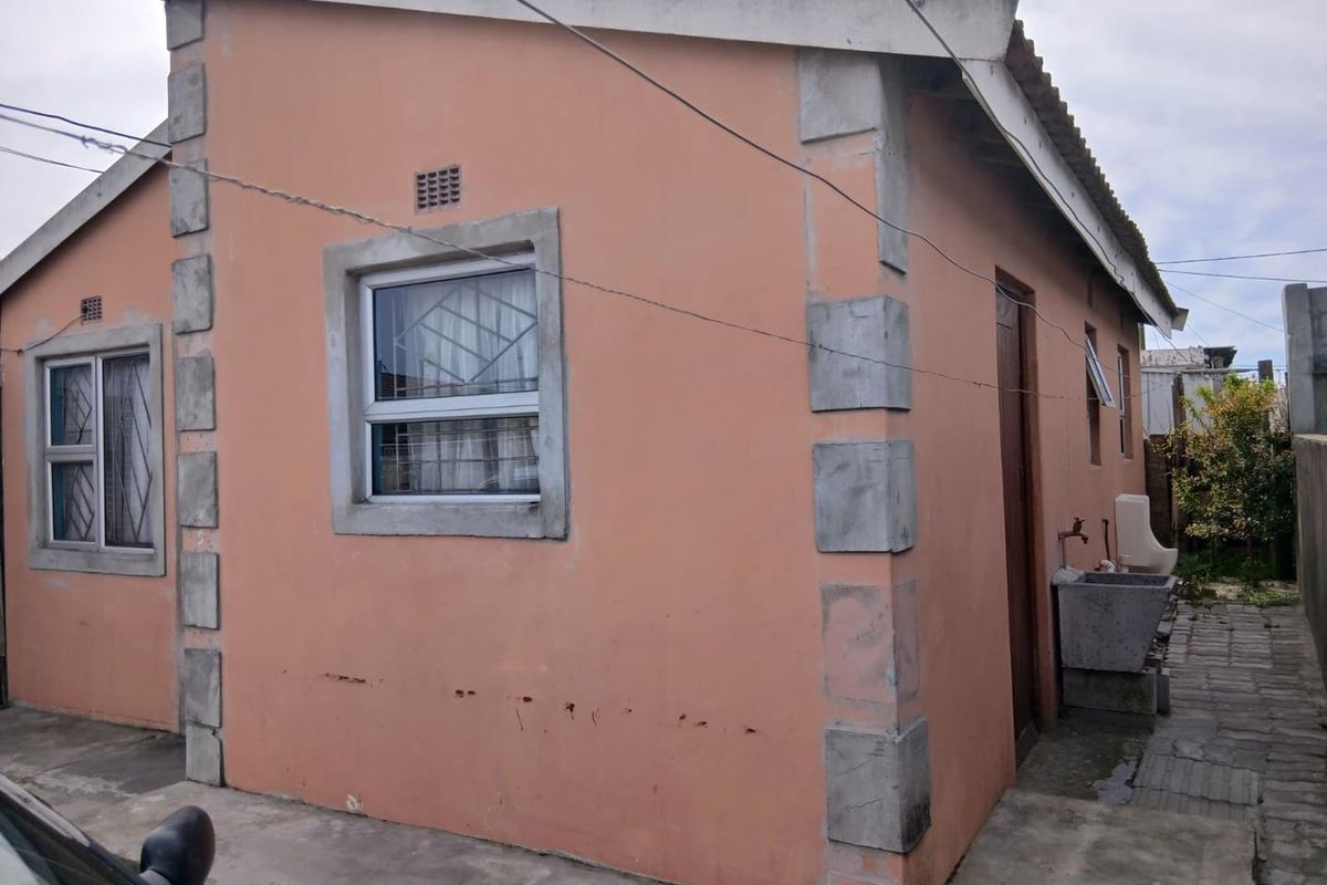 Rear exterior view of the house featuring concrete corner detailing, an external wash basin, and aluminium window frames with security bars.