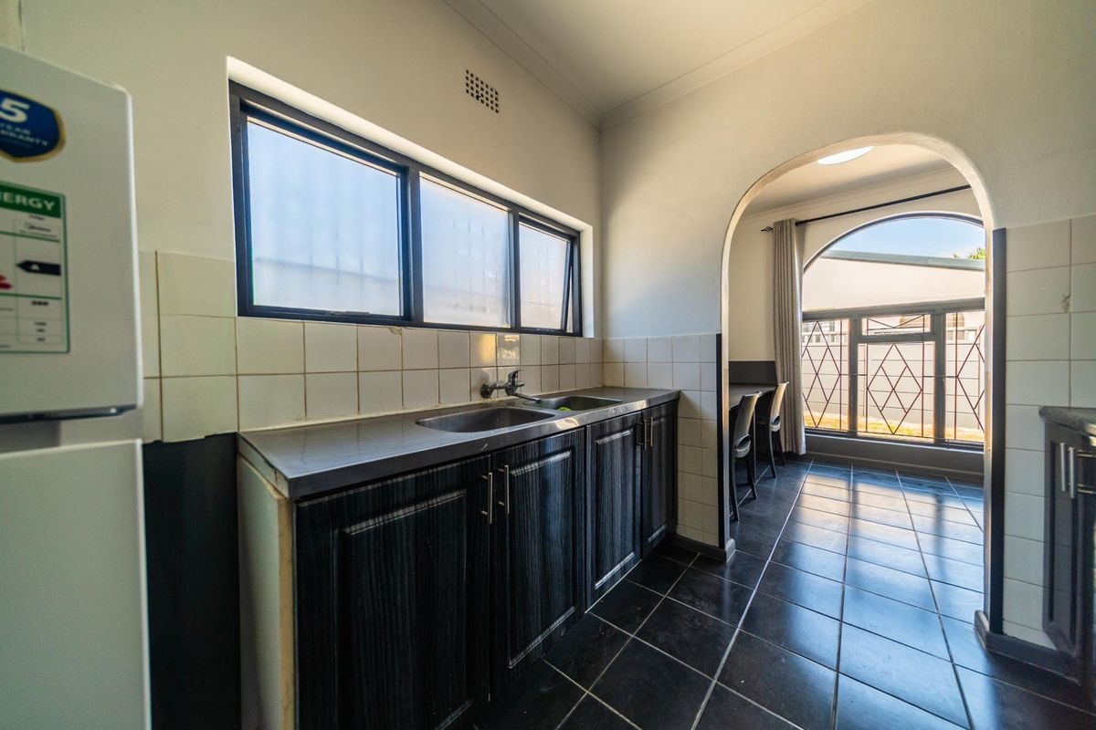 A functional kitchen area featuring dark cabinetry, a stainless steel sink, tiled backsplash, and dark floor tiles, leading through an archway to an adjacent space.