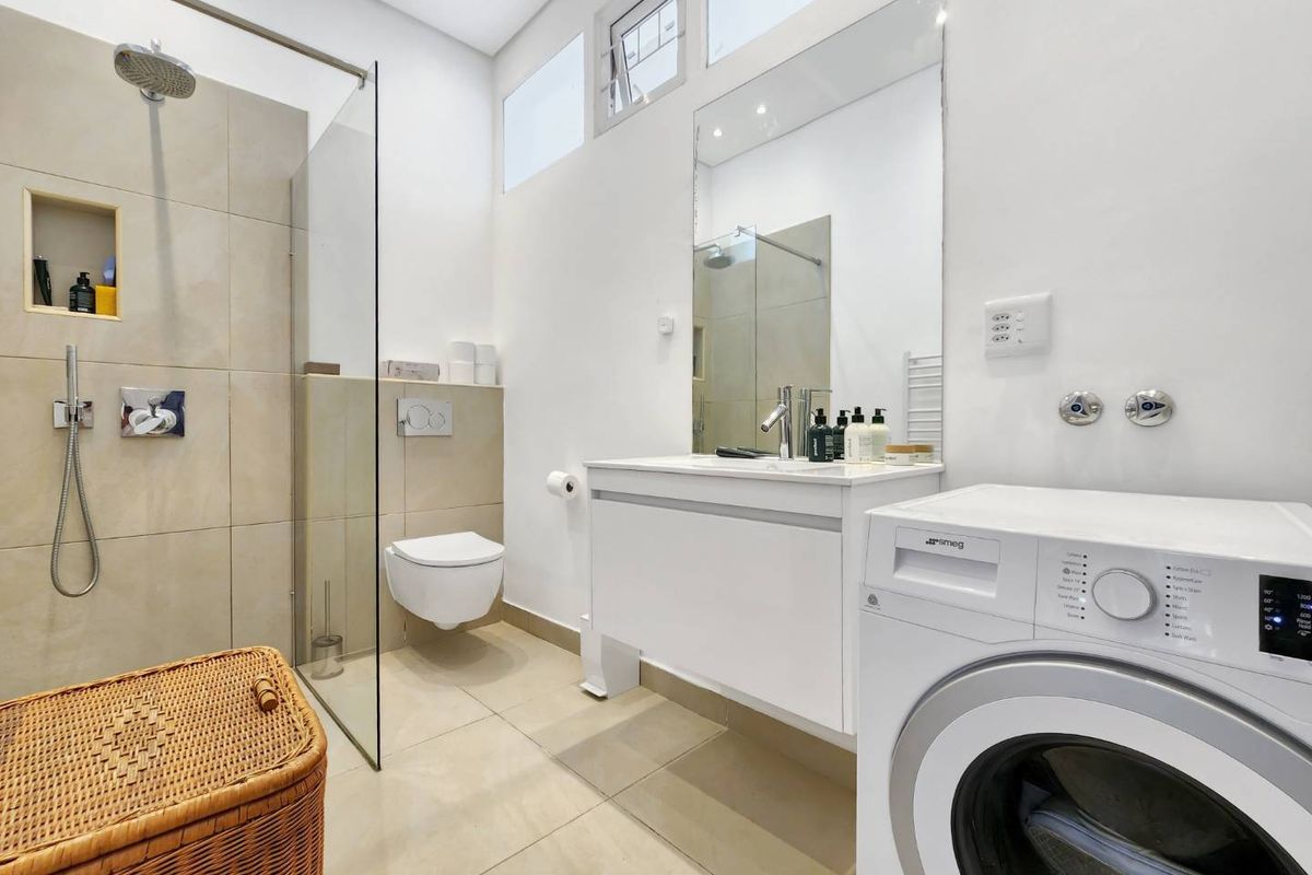 Modern bathroom featuring a walk-in shower with glass screen, wall-mounted toilet, vanity with integrated mirror, and tiled finishes throughout.
