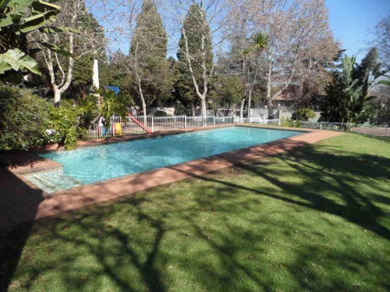A rectangular swimming pool set within a landscaped garden, featuring brick coping and secure perimeter fencing.