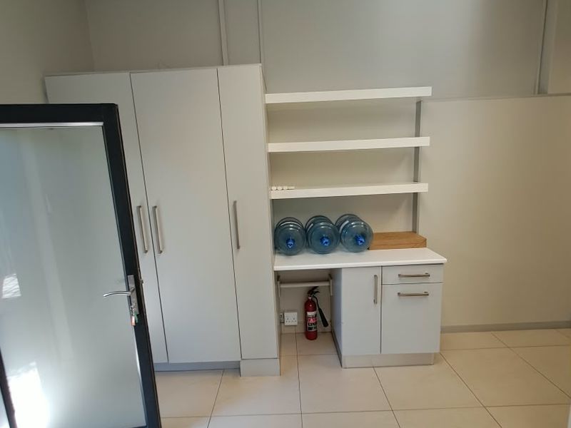 A clean, functional office space featuring built-in storage cabinetry, open shelving, and neutral tiled flooring, suitable for a professional work environment.