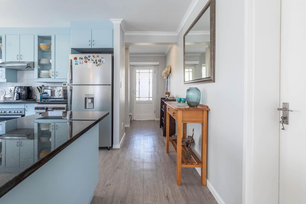 A bright kitchen featuring light blue cabinetry, dark granite countertops, and wood-look flooring, leading into a hallway with a glass-paneled exterior door.