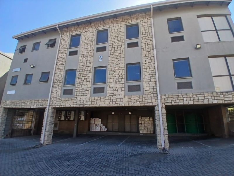 Front elevation of a multi-story commercial building featuring stone cladding, paved parking area, and integrated air conditioning units.