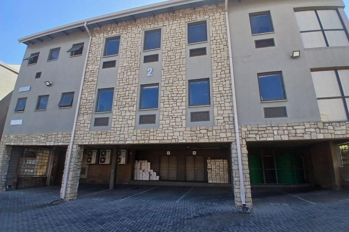Front elevation of a multi-story commercial building featuring stone cladding, paved parking area, and integrated air conditioning units.
