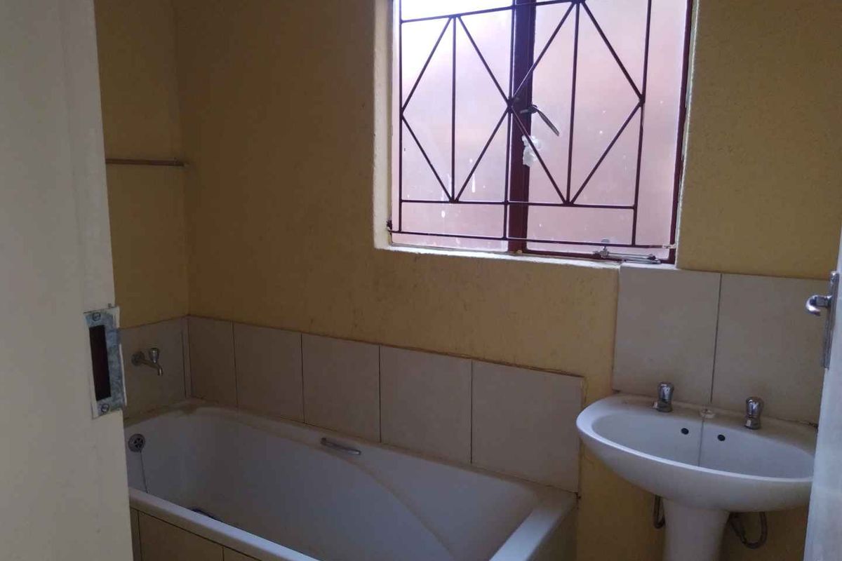 A compact bathroom featuring a standard bathtub, pedestal basin, and a window with security bars, requiring cosmetic updates to modernize the space.